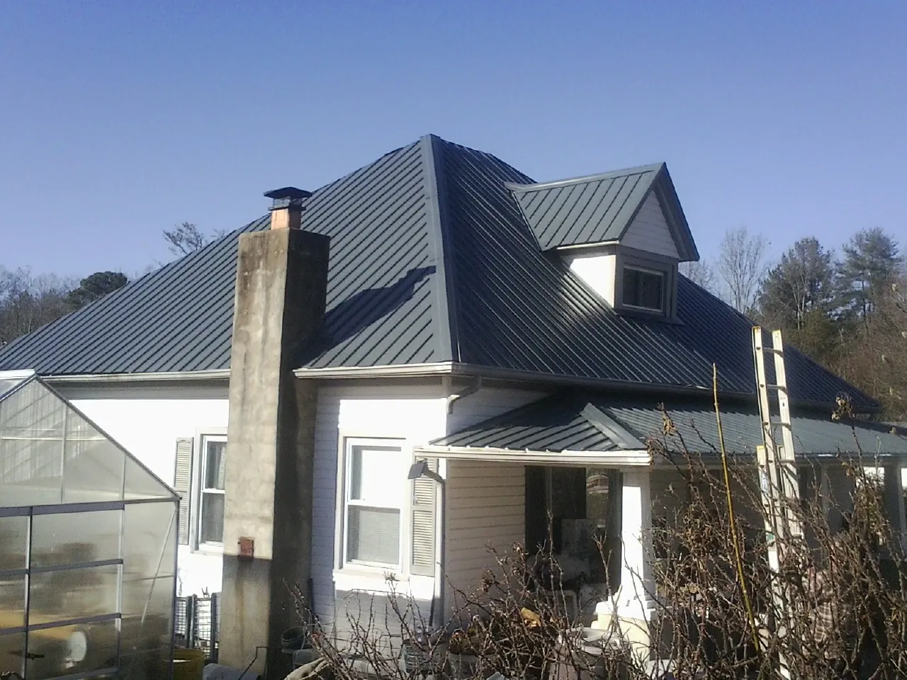 Dark blue standing seam metal roof on a white farmhouse with dormer — Slate & Tile Roof Repair by Roofing Brothers in Roanoke