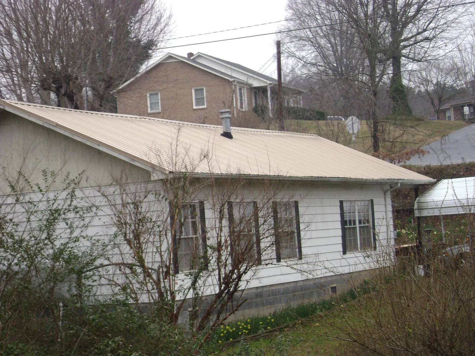 Tan metal roof on a white sided house set into a hillside — Commercial Roofing by Roofing Brothers in Roanoke